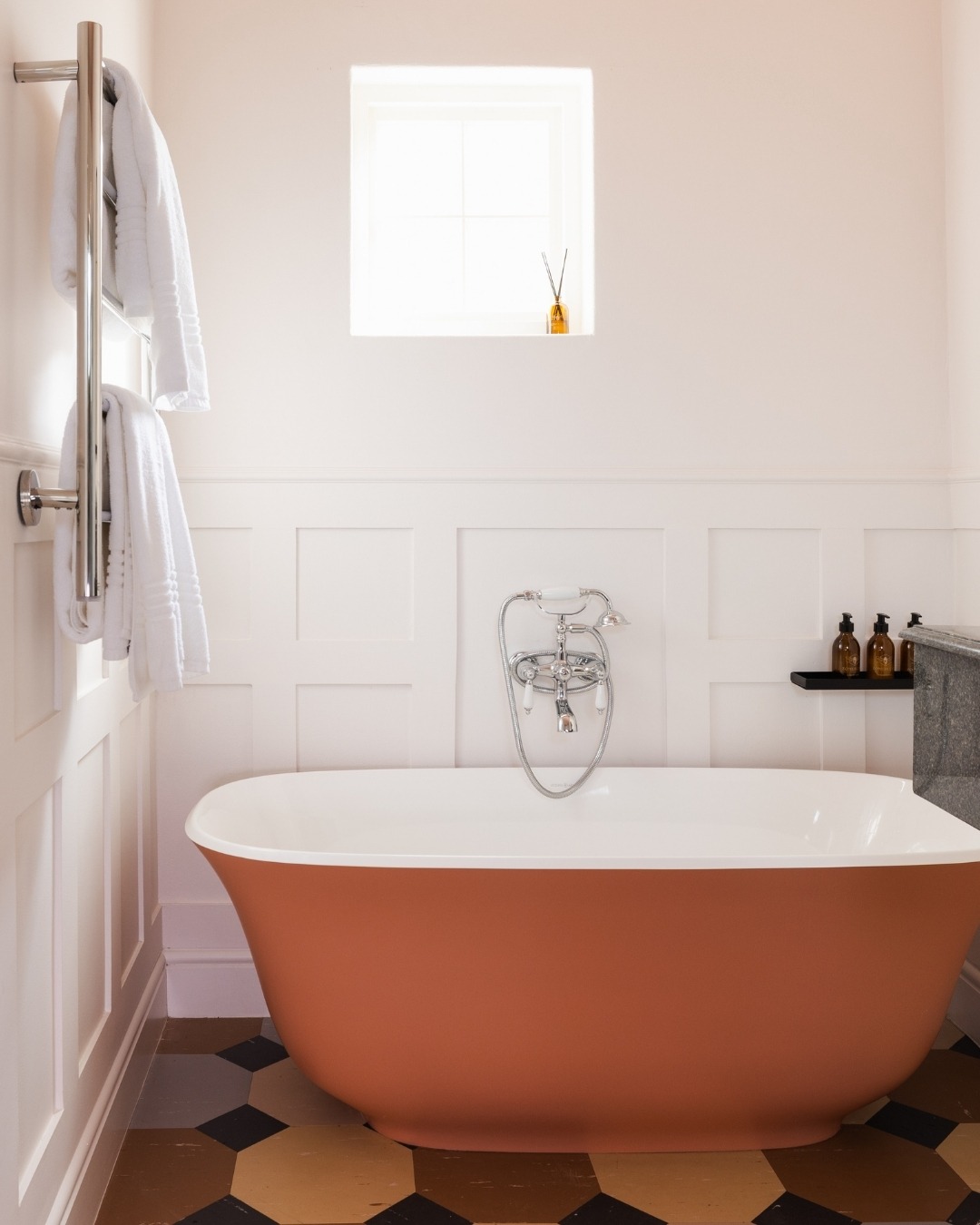 Zomerlust Boutique Hotel Paarl. Terracotta-colored freestanding bathtub in a modern bathroom with white wainscoted walls, chrome fixtures, geometric floor tiles, and a heated towel rack.